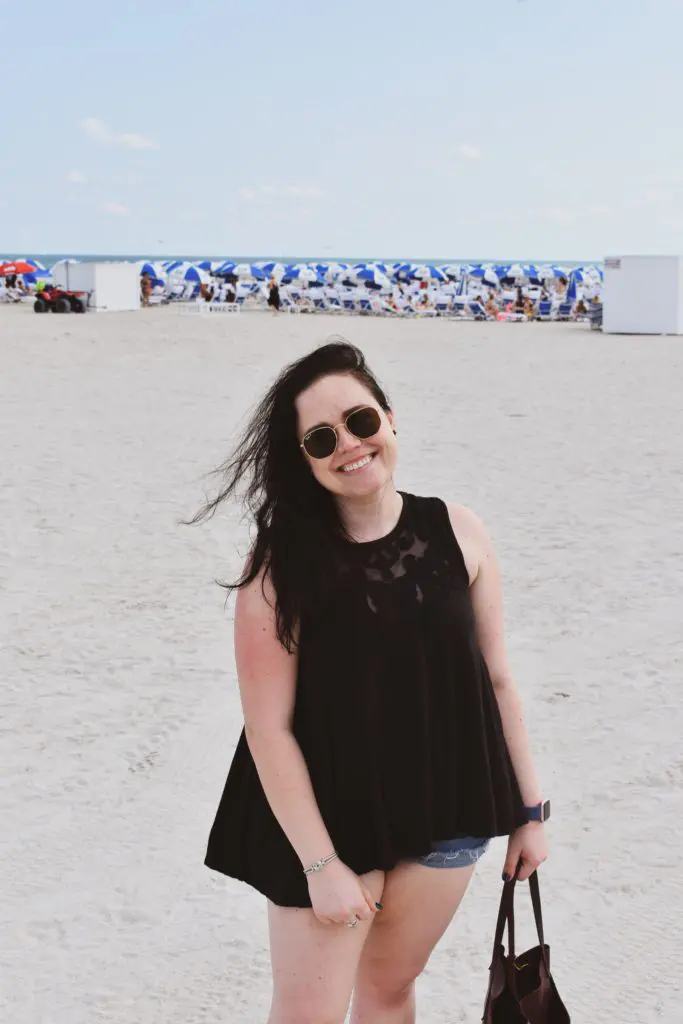 South Beach - Cats & Coffee Christine Csencsitz standing on the beach with a Free People top, J. Crew shorts, and a Madewell purse.