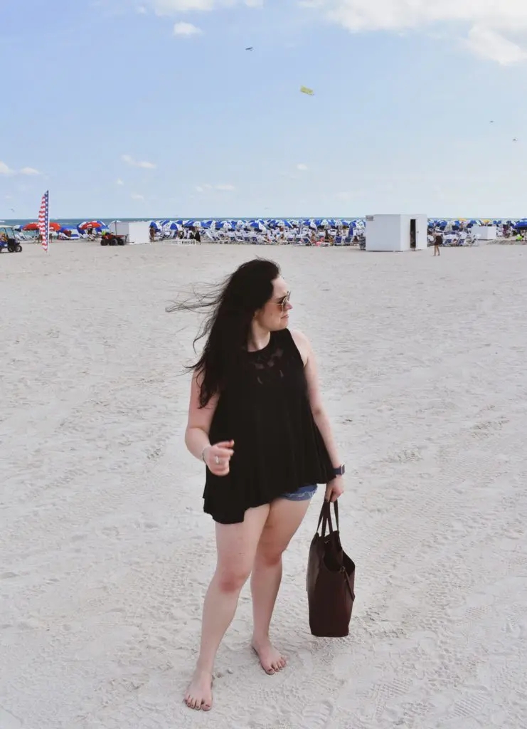 South Beach - Cats & Coffee Christine Csencsitz standing on the beach with a Free People top, J. Crew shorts, and a Madewell purse.