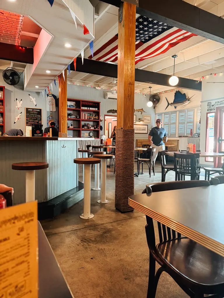 Cheekys St Pete Restaurant Clam Bar 1 - Cats & Coffee Casual cafe interior with a long counter, wooden posts wrapped in rope, and tables for seating under string lights and an American flag overhead.