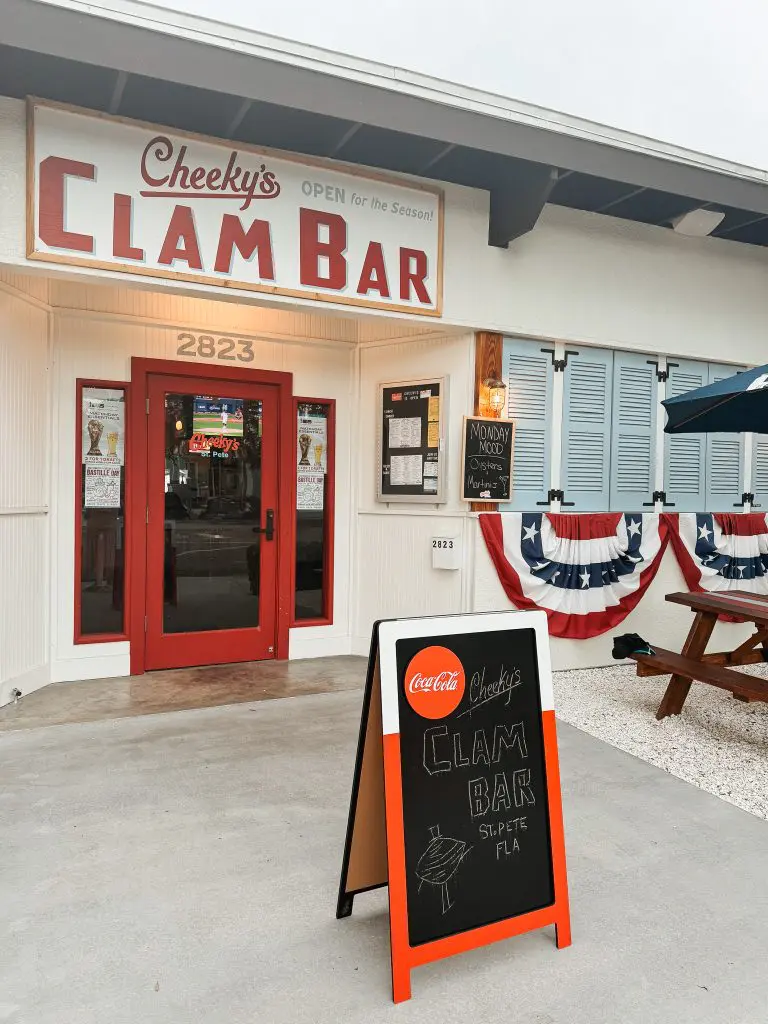 Cheekys St Pete Restaurant Clam Bar 3 - Cats & Coffee Exterior view of Cheeky's Clam Bar storefront with a red door, large sign, chalkboard menu, and patriotic bunting.
