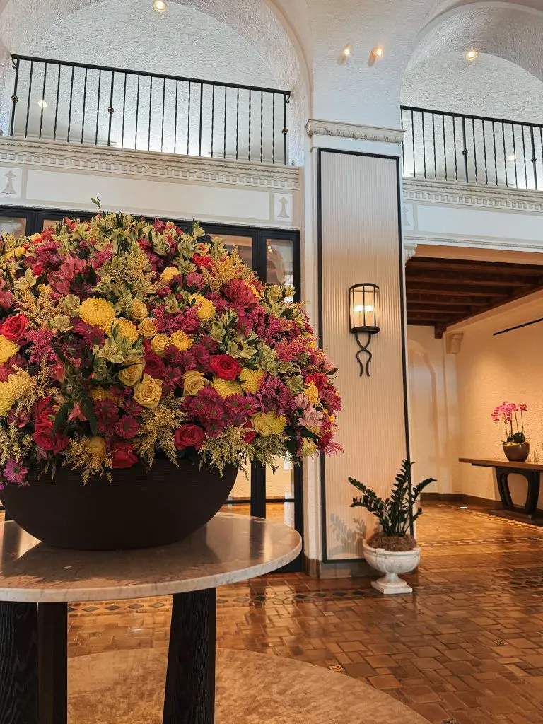 The Vinoy St Pete - Where to Stay in Tampa Bay - 3 - Cats & Coffee Large round black planter on a marble table holds a vibrant bouquet of pink, yellow, and purple flowers in an elegant indoor lobby.