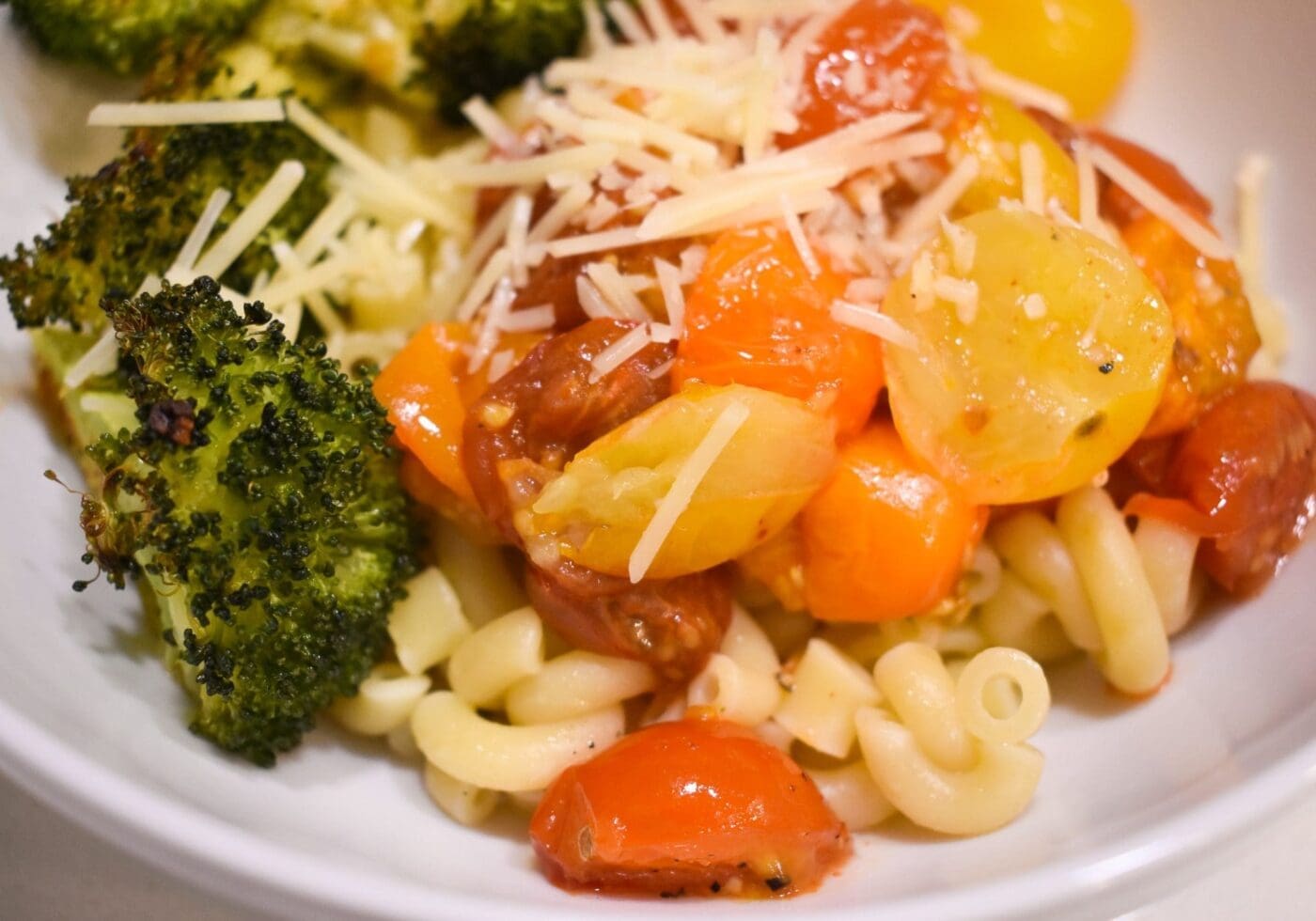 Plated Pomodoro pasta with roasted broccoli and shredded parmesan cheese.