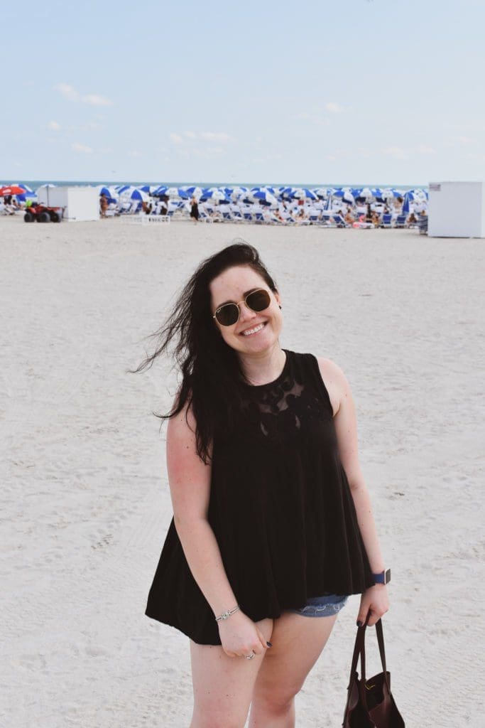 Christine Csencsitz standing on the beach with a Free People top, J. Crew shorts, and a Madewell purse. 