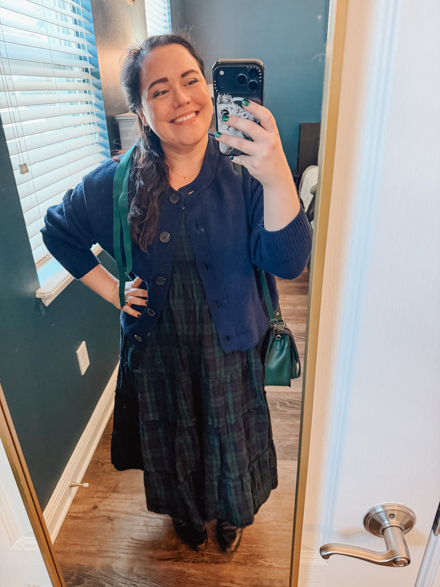 Festive-Tartan-Outfit-Ideas-7-Ways-to-Wear-Tartan-This-Holiday-Season-6webp - Cats & Coffee Woman wearing black and green tartan dress layered with navy blue cardigan and green crossbody bag — cozy dressy tartan outfit