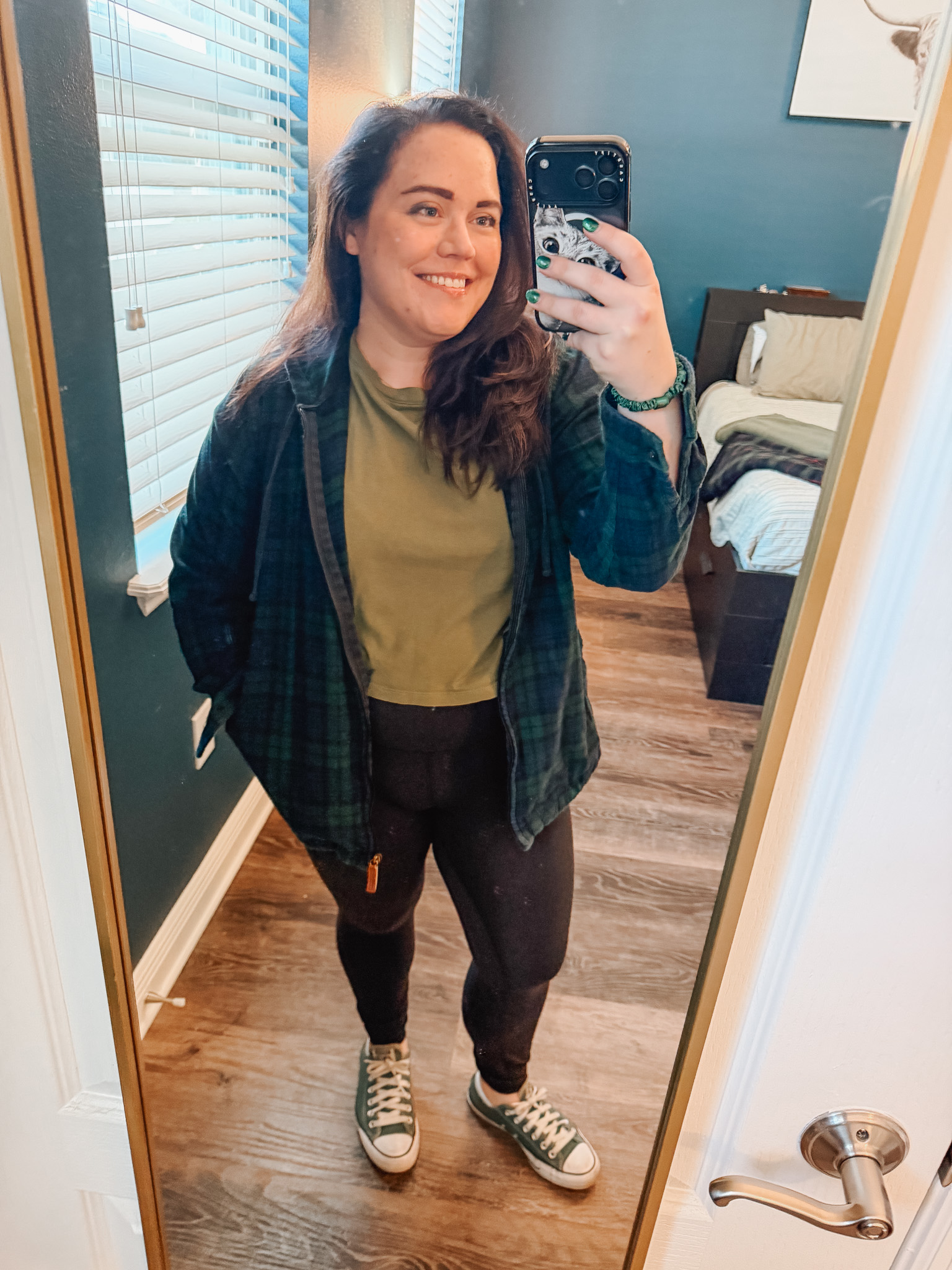 Festive-Tartan-Outfit-Ideas-7-Ways-to-Wear-Tartan-This-Holiday-Season-7webp - Cats & Coffee Woman wearing green and black tartan plaid shacket over olive tee with black leggings and Converse — casual layered tartan look for travel